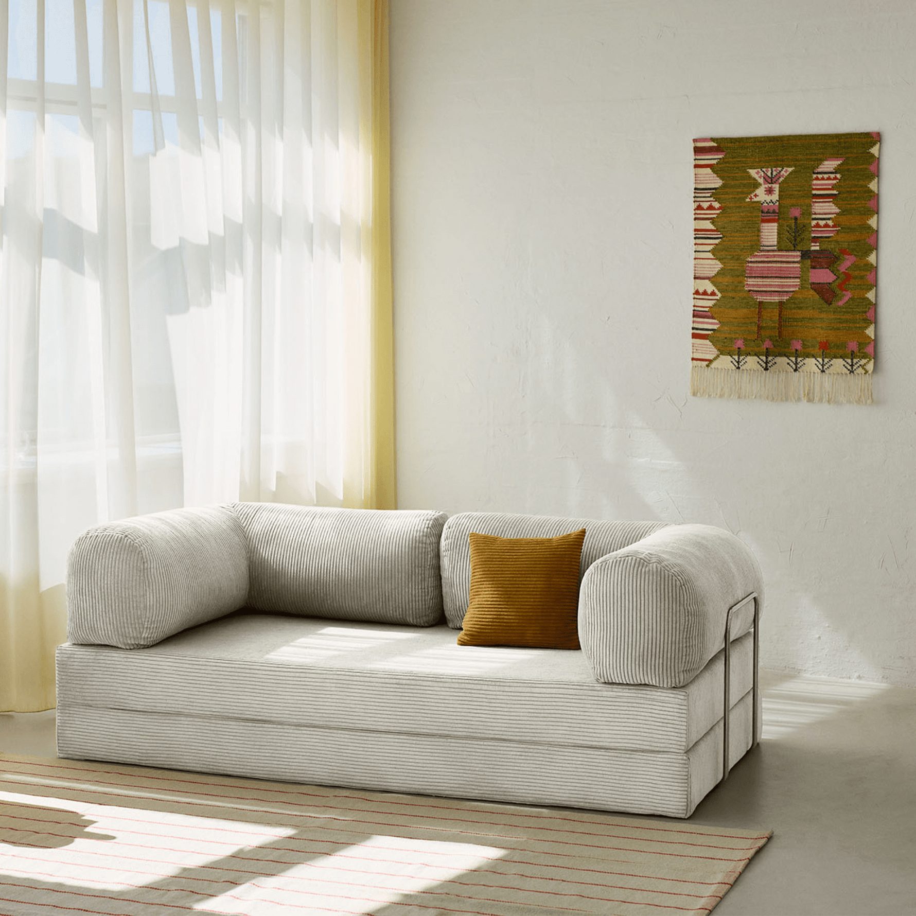 Primyhome white corduroy convertible sofa bed in a sunlit living room with minimalist decor and boho wall art